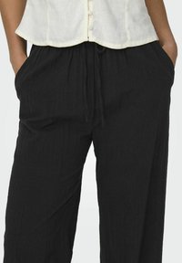 Pantalons en lin noirs à coupe décontractée, dotés d'une taille élastique et d'un cordon de serrage, ainsi que de deux poches latérales. Tissu texturé subtil.
