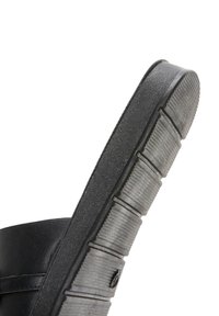 Zapato negro con parte superior de cuero texturizado y una suela de goma gruesa y estriada, que muestra un perfil lateral suave y una puntera redondeada.
