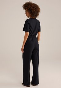 Zwart jumpsuit met korte mouwen, elastische taille en brede pijpen. Zachte textuur, minimale details, en gecombineerd met dierenprint ballerina's.
