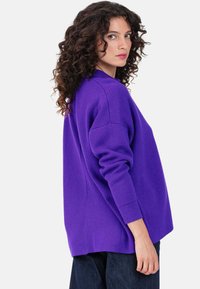 Pull oversize violet à manches longues, avec col et poignets en côtes, associé à un jean en denim foncé, en maille texturée.