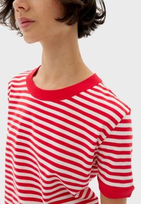 Rode en witte gestreepte t-shirt met een ribgebreide halslijn en korte mouwen. De stof lijkt zacht met een gladde textuur.
