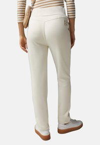 Witte sweatpants met een brede elastische tailleband, voorzien van subtiele zakken en een logo-detail op de achterkant. Draagt met witte sneakers.