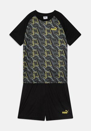 Conjunto atlético negro que incluye una camiseta de manga corta con un patrón geométrico dinámico en gris y amarillo, y pantalones cortos negros a juego.