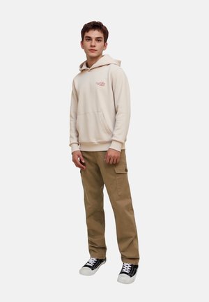 Cream hoodie with front pocket, red printed logo, paired with loose beige cargo pants and black sneakers with white soles.