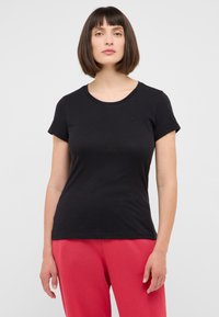 T-shirt noir à manches courtes, col rond, en tissu doux, design ajusté, détail logo subtil sur la poitrine, associé à un pantalon rose.