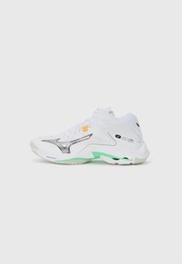 White athletic shoe with black and silver accents, green sole detail, textured overlays, and orange tab; curved design for support and flexibility.