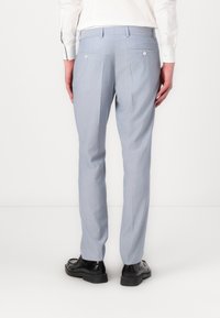 Pantalones azul claro con corte ajustado, que presentan dos bolsillos traseros con botones y una raya en la parte frontal. Combinados con zapatos negros.