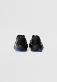 Des chaussures de sport noires présentent une tige texturée, des accents bleus, et une semelle noire épaisse avec un détail de semelle extérieure bleue.