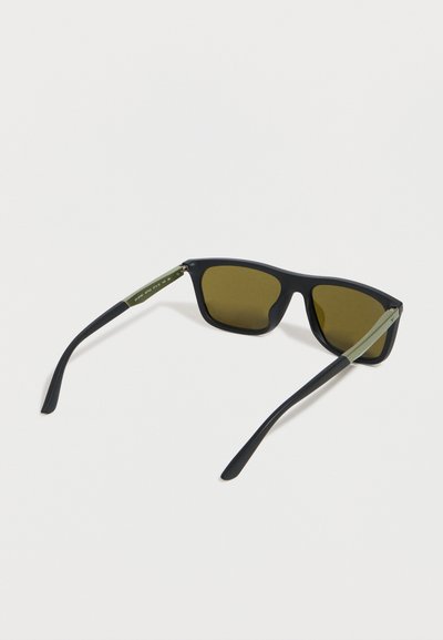 Μαύρα ορθογώνια γυαλιά ηλίου με ελαιόλευκα βραχίονες και φακούς με καφέ απόχρωση, ανοιχτά τοποθετημένα πάνω σε λευκή επιφάνεια.