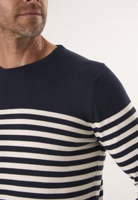 Marineblauwe trui met horizontale witte strepen, gemaakt van een zachte stof. Voorzien van een ronde halslijn en fitted mouwen.