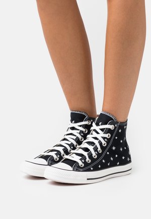 Sneaker alte nere in tela, con motivi a stelle bianche, lacci bianchi e suole in gomma con accenti neri.