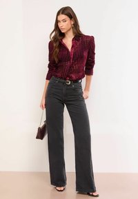 Burgundijas pārbaudīta pogu krekls ar garām piedurknēm, apvienots ar augsta jostasvieta melniem platajiem džinsiem un melniem zābakiem ar papēžiem.