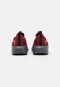 Punainen urheilukenkä, jossa on teksturoitu päällinen, mustat pohjat, kullanvärisiä yksityiskohtia ja takana vetolenkit helppoa pukemista varten. "Better Foam" -brändäys näkyvissä.