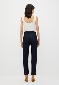 Vaqueros de denim azul oscuro con corte recto, cinco bolsillos y una cinturilla limpia. Combinados con una camiseta de tirantes blanca con canalé.