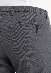 Tmavě modré kalhoty s texturou, úzkým střihem, diagonálním vzorem tkaní a zadní kapsou s malým koženým detailem.