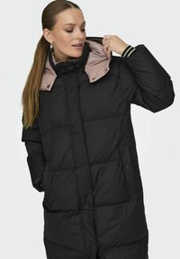 Svart puffjakke med høy krage og kontrastfarge i lys rosa fôr. Har quiltet polstring og knappelukking, laget av syntetisk materiale.