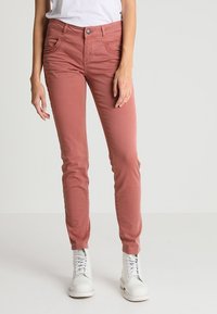 Růžové slim-fit džíny s pěti kapsami, prošitými detaily a zapínáním na knoflík, nošené s bílými šněrovacími botami.