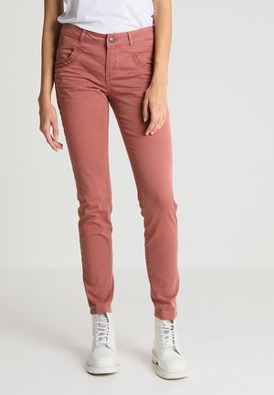 Růžové slim-fit džíny s pěti kapsami, prošitými detaily a zapínáním na knoflík, nošené s bílými šněrovacími botami.