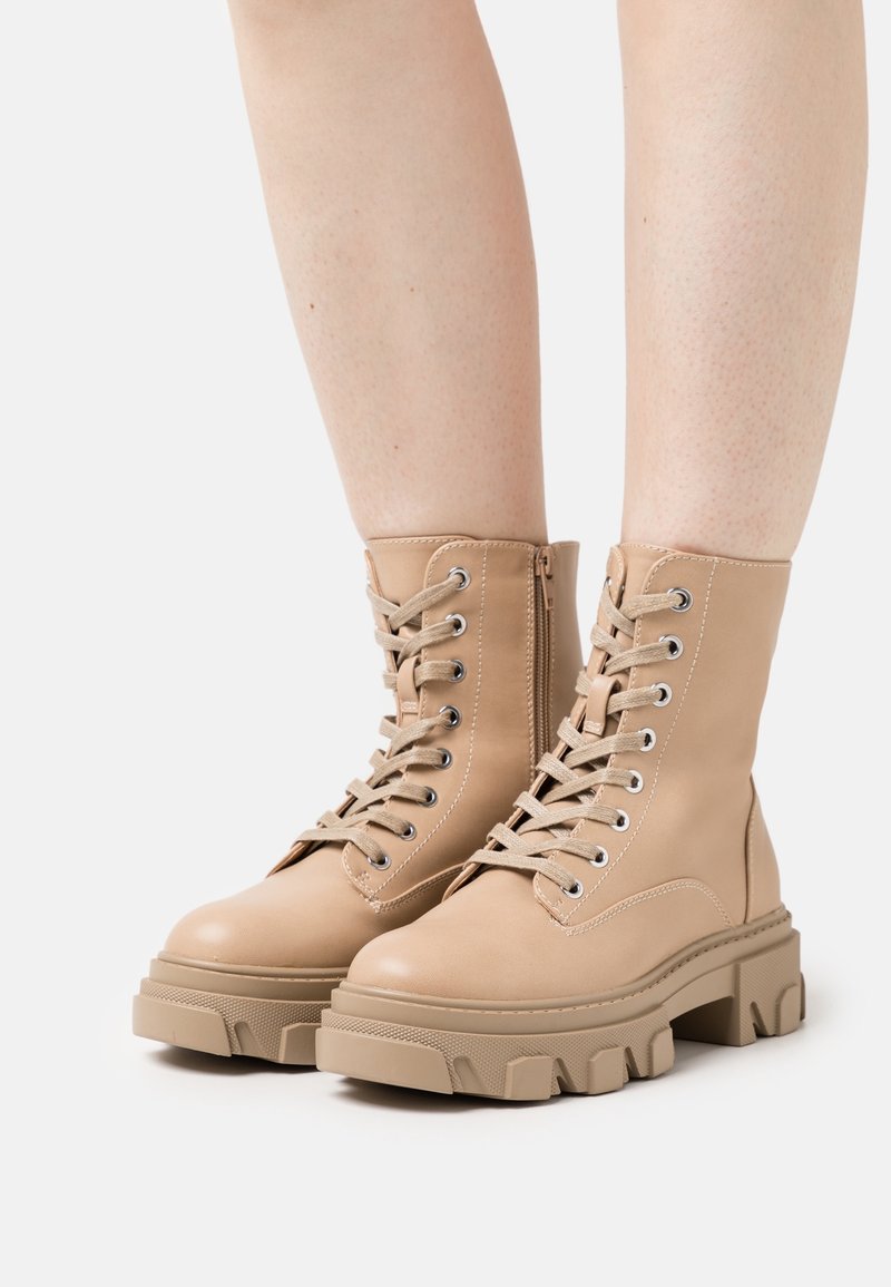 Bottes de combat en cuir beige avec une semelle épaisse, dotées d'œillets métalliques, de lacets épais et d'une fermeture éclair latérale pour un enfilage facile.