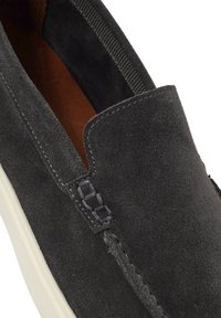 Zapatilla tipo slip-on de ante gris oscuro con un acento de costura y suela blanca contrastante. El interior está forrado en cuero marrón. Incluye paneles laterales elásticos.