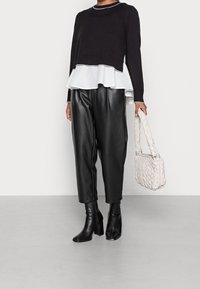 Black knit sweater with white ruffled peplum hem, paired with black faux leather trousers and black heeled boots. Features a woven light grey handbag.