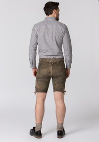 Braune Lederhosen mit seitlichen Schnürungen, kombiniert mit einem karierten Hemd. Das Hemd hat einen Button-Down-Kragen und lange Ärmel.