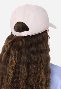 Šviesiai rožinė beisbolo kepuraitė su išlenktu snapeliu, reguliuojamu dirželiu gale ir ventiliacijos skylutėmis; tekstūruota medžiaga su matomomis siūlėmis.