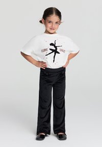 Biała koszulka z czarnym siluetą tancerki baletowej i błyszczącym tekstem, połączona z czarnymi spodniami w katedralne prążki i błyszczącymi czarnymi baletkami.