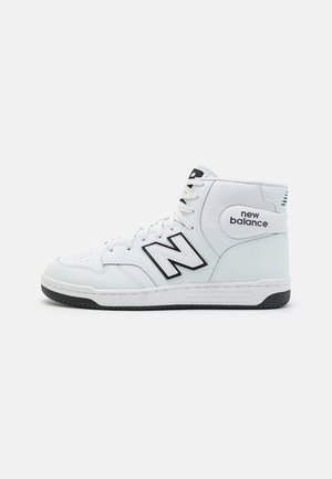 White high-top New Balance sneaker with black logo and sole accents, showing side profile against a plain light background.