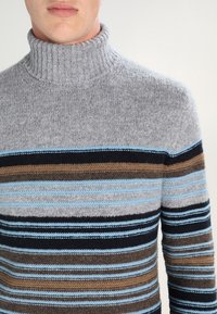 Šed ý rolákový svetr s vodorovnými pruhy v modré, hnědé a černé barvě. Pletená textura s žebrovaným výstřihem a lemy na rukávech.