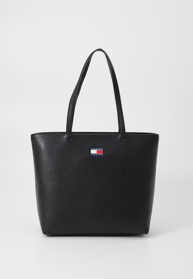 Schwarze Leder-Totetasche mit strukturierter Oberfläche, ausgestattet mit zwei Schulterriemen und einem kleinen Logo-Patch in Rot, Weiß und Blau auf der Vorderseite.