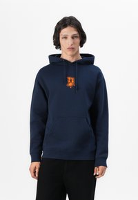 Sweatshirt azul-marinho com bolso frontal, capuz com cordão e um logótipo laranja no peito. Feito de tecido suave, apresentando um ajuste padrão.