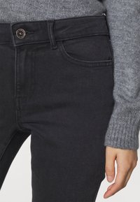 Svarta denimjeans med en åtsittande design, med knappstängning, framfickor och subtila sömnadsdetaljer. Åtföljd av en gråstickad tröja.