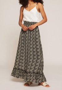 Czarna i biała kwiatowa spódnica maxi z falbanym dołem, w połączeniu z białą bluzką na ramiączkach i jasnymi sandałami.