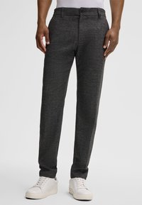 Pantaloni grigi con una texture, dal taglio slim, con chiusura a bottone e tasche laterali, abbinati a sneaker bianche.