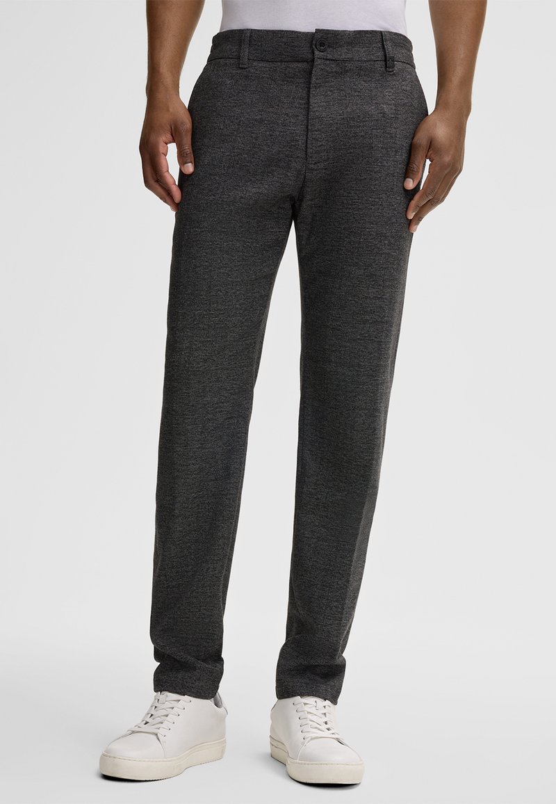 Pantaloni grigi con una texture, dal taglio slim, con chiusura a bottone e tasche laterali, abbinati a sneaker bianche.