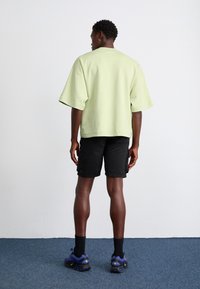 Light green oversized sweatshirt with short sleeves, paired with black shorts, blue sneakers, and black socks. Simple design, casual fit.