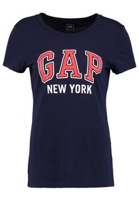 Námořnická modrá tričko s krátkým rukávem vyrobené z bavlny, s tučným červeným a bílým nápisem "GAP" a "NEW YORK". Design s výstřihem do V.