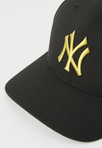 Gorra negra con visera plana, que presenta un destacado logo bordado en oro de NY en la parte delantera. Hecha de un material texturizado, que muestra un detallado bordado.