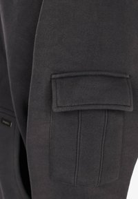 Sötétszürke anyag, téglalap alakú hajtókájával, amelyen függőleges varrásvonalak találhatók egy ruhaujjon.