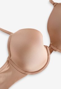 Glat, sømløs nude-farvet polstret BH med bøjle og justerbare stropper, lagt fladt på en hvid baggrund.