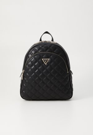 Sac à dos en cuir matelassé noir avec poche avant zippée et logo Guess doré sur fond blanc uni.