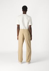 Beige wide-leg pants with a loose fit, made from durable fabric, featuring two back pockets and visible stitching details.