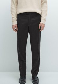 Kolsvartra byxor med en elegant design, som har en skräddarsydd passform och subtil textur. Kombineras med en krämfärgad ribbad stickad tröja och svarta loafers.