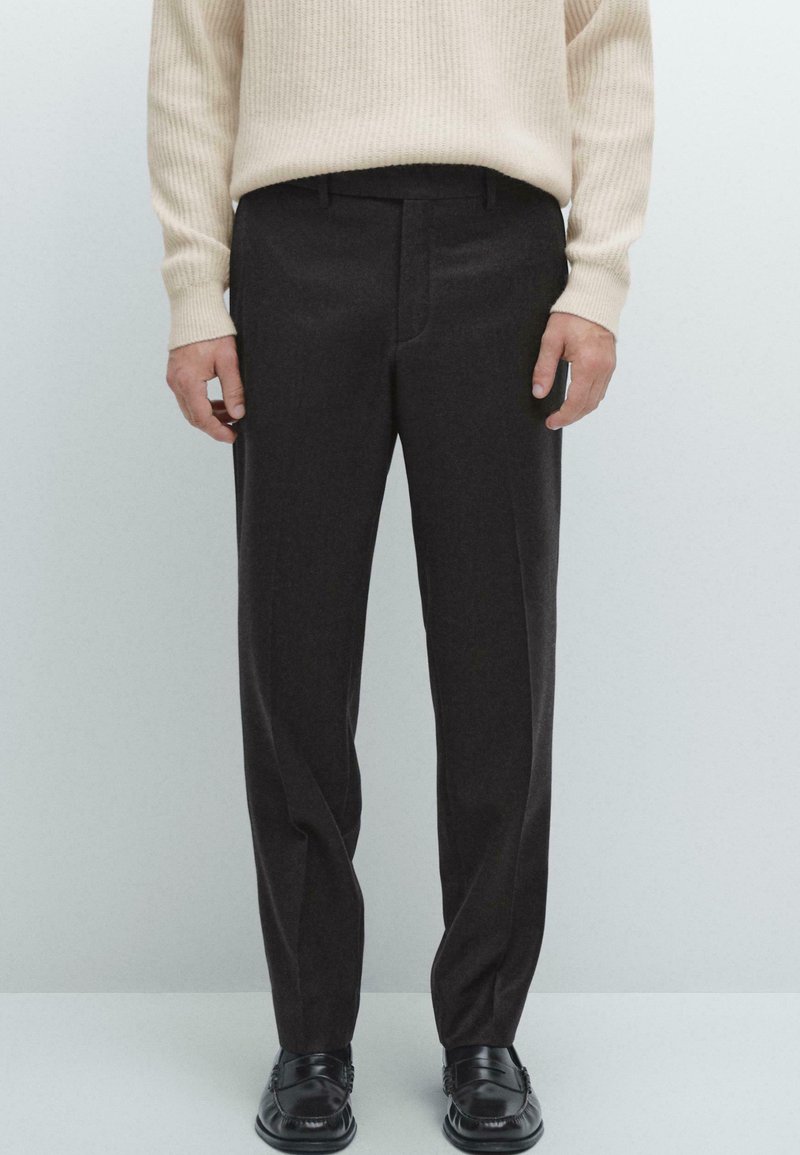 Kolsvartra byxor med en elegant design, som har en skräddarsydd passform och subtil textur. Kombineras med en krämfärgad ribbad stickad tröja och svarta loafers.