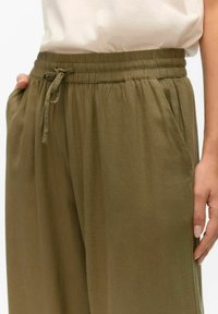 Pantalones ligeros de color verde oliva, con cintura elástica y cordón, y bolsillos laterales, que presentan una textura suave y un ajuste relajado.
