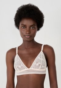 Triangle bralette in soft beige lace with floral patterns, sheer detailing, and adjustable straps. Features a textured underband for support.