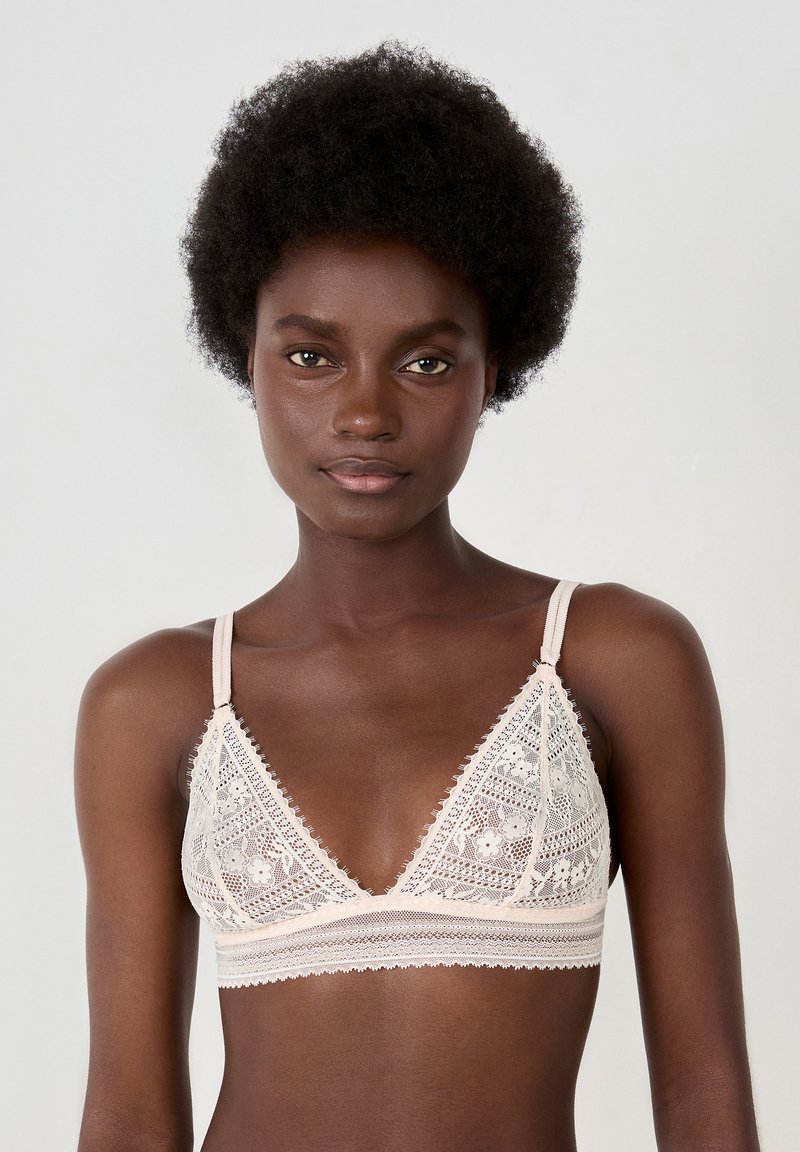 Bralette a triangolo in pizzo beige morbido con motivi floreali, dettagli trasparenti e spalline regolabili. Presenta un sottobanda testurizzato per supporto.