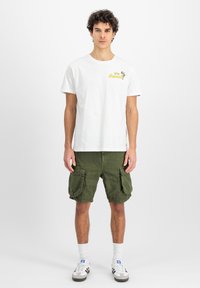 Hvid bomulds t-shirt med gult trykt tekst, parret med olivengrønne cargo shorts med flere lommer, hvide sokker og grå sneakers.