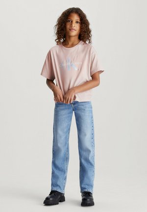 Camiseta de algodón de color rosa claro con logo impreso, combinada con jeans de denim azules. Unos zapatos negros de suela gruesa completan el conjunto.